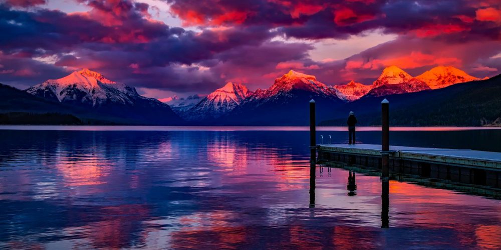 Stunning sunset over a serene lake with colorful sky and majestic mountains.