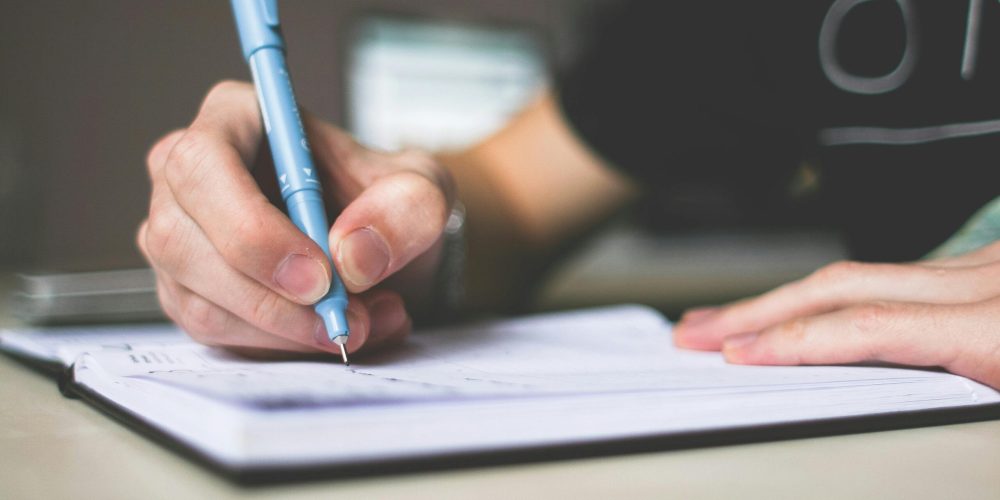 Close-up of hand writing in notebook using a blue pen, focus on creativity.