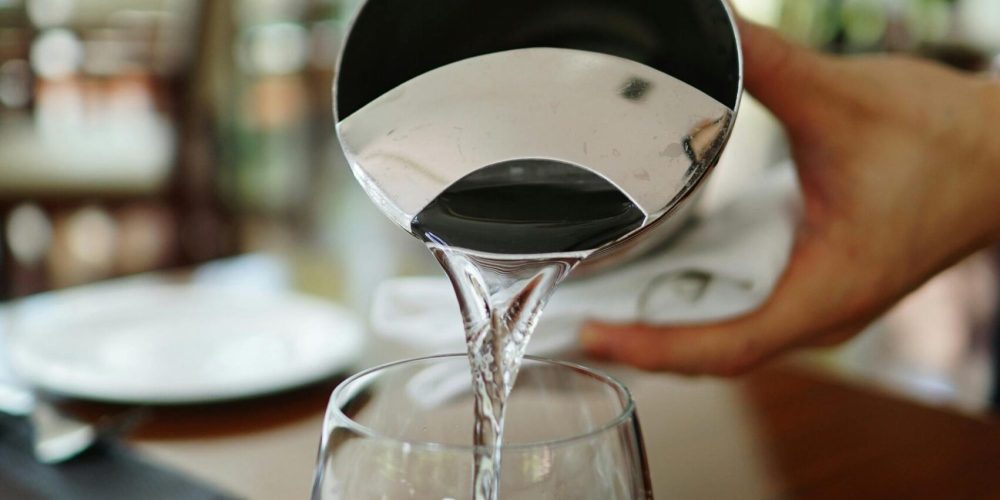 Close-up of water being poured into a glass in a restaurant setting.